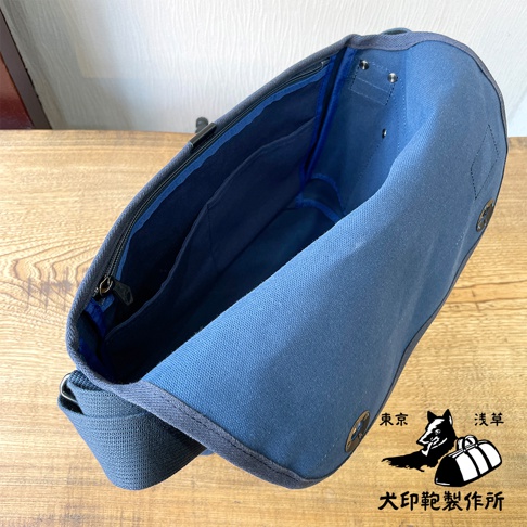 海軍藍純棉帆布雙扣郵差包，內有隔層，包身有金屬扣眼，左側有東京淺草犬印鞄製作所的標誌。
