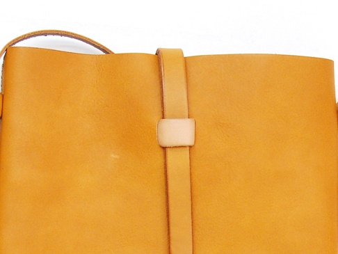 職人手作皮革散步直式單肩包 (CP-3)，以柔軟的黃褐色皮革製成，簡潔的設計，正面有皮革束帶與固定扣，肩帶亦為皮革材質。