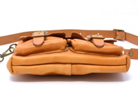 職人手作皮革水洗加工前雙口袋肩背包，呈現自然的淺棕色皮革，包身有兩個翻蓋式前袋，配備金屬扣環和可調式皮革背帶。