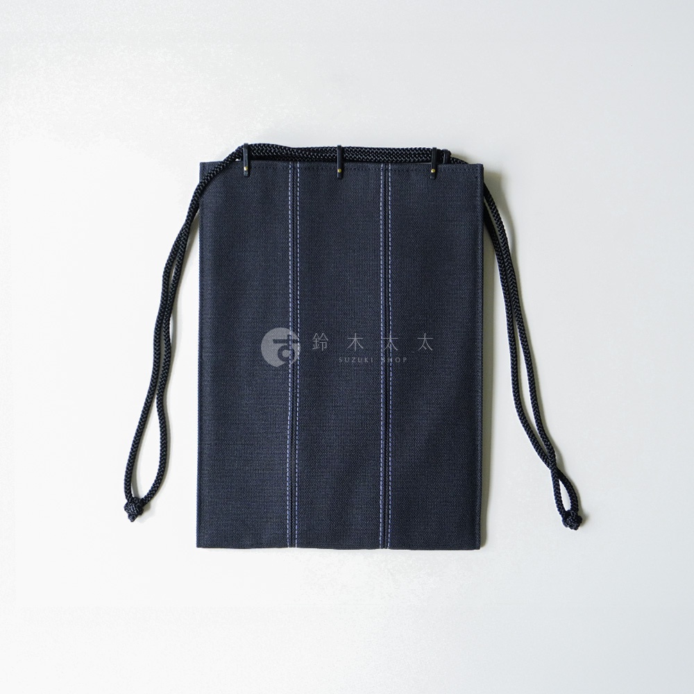 正面俯視拍攝一個深藍色帆布材質的信玄袋，袋身以兩條淺色縱向縫線裝飾，上方配有黑色編織繩作為提把，中央印有白色圓形圖標與鈴木太太 SUZUKI SHOP 的品牌字樣，整體設計簡約具日式風格。