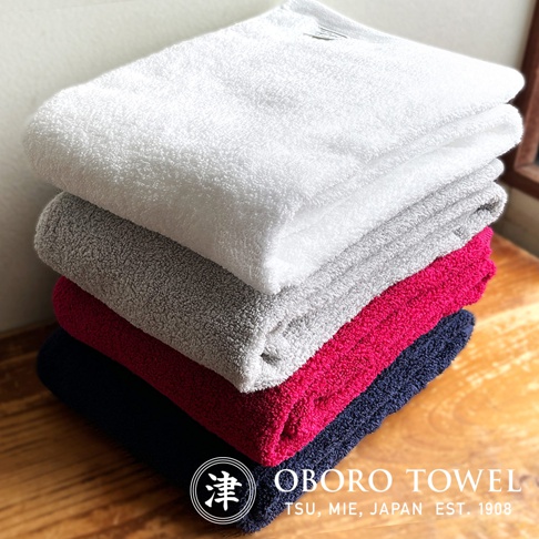 堆疊的細纖浴巾，顏色包含白色、灰色、桃紅色和海軍藍，材質呈現蓬鬆柔軟的觸感。