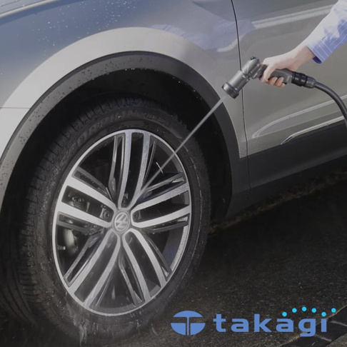 銀色汽車的輪胎和車身側面，手持灰色噴水槍噴灑水柱，水花濺射在車輪上。