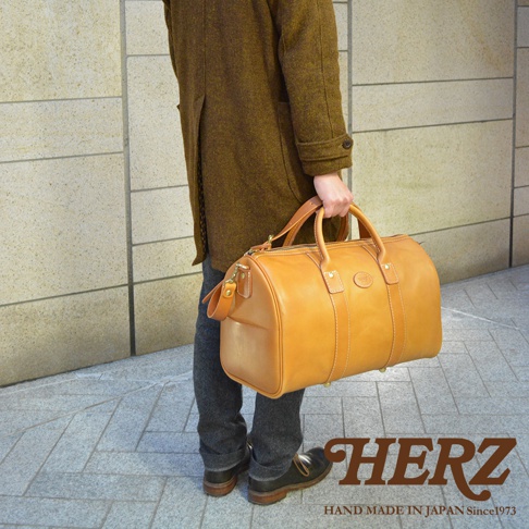 職人手作皮革肩背手提拉鍊波士頓包，採用天然棕色皮革製成，配有堅固的提把和可拆卸肩帶。包款的拉鍊設計方便取物，側邊有金屬腳釘，整體風格經典實用。