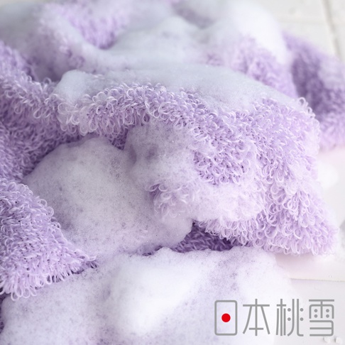 淡紫色綿柔沐浴巾，帶有豐富的白色泡沫，材質呈現細緻的捲曲紋理。