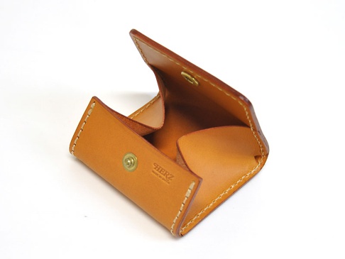 淺棕色皮革製成的箱型零錢包，打開狀態，露出內部空間，有金色按扣及品牌標誌。