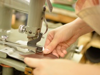 職人使用皮革裁切機，將深棕色皮革裁切成形，用於製作存摺文件收納夾。