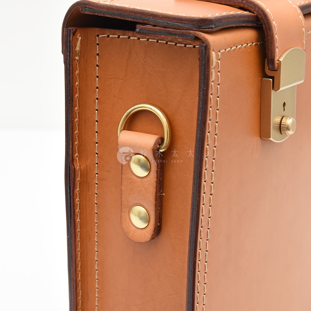 職人手作皮革兩用機師箱，淺棕色皮革，配有金色金屬鎖扣、旋鈕及兩顆鉚釘固定的皮質掛環，縫線清晰。