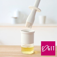 白色矽膠刷毛沾取玻璃罐中的黃色液體，下方為透明玻璃罐裝有淺黃色油，罐身外層為白色外殼，背景為淺色調。