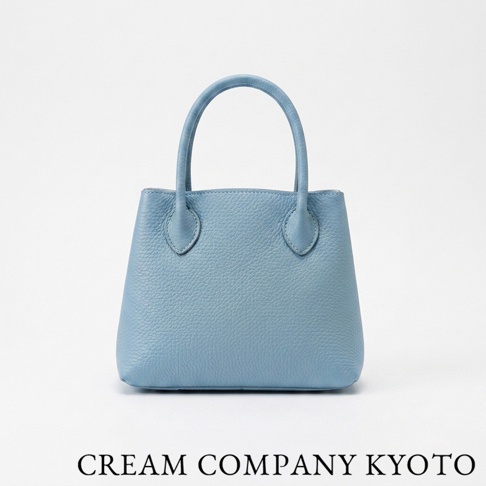 這是一款由日本京都職人手作的 CREAM COMPANY KYOTO 皮革手提托特包，呈現簡約優雅的淺藍色調，採用輕量耐用的 glove 牛皮製成，表面具有細緻的荔枝紋路，正面下方印有品牌名稱。