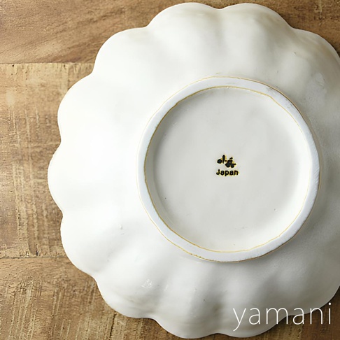 一個白色的陶瓷主食盤，邊緣有花瓣狀的波浪紋，盤底印有「小兵」的日文標誌和「Japan」字樣。