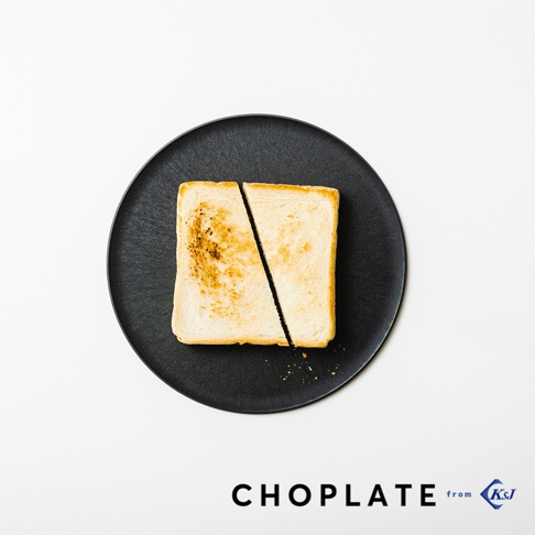 黑色圓形砧板盤上放著一片切成兩半的吐司，吐司表面烤至金黃，部分區域略帶焦色。