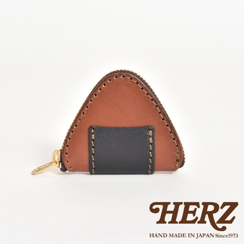 日本職人手作HERZ皮革零錢包，外型設計成可愛的三角飯糰造型，採用棕色皮革搭配黑色皮革細節，邊緣飾有細緻手工縫線，側面配有金色拉鍊，整體呈現簡約精緻的質感。