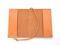 職人手作皮革附繩書套，淺棕色皮革，有縫線裝飾，中央有三條皮革綁帶，左側皮革內印有「HERZ」品牌標誌。