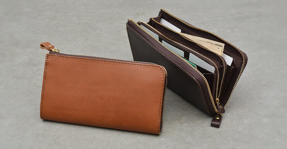 兩款職人手作皮革拉鍊長夾，一款為棕褐色皮革，另一款為深棕色皮革，內部裝有卡片及鈔票。