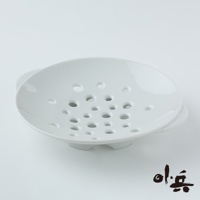 白色陶瓷美濃燒多用蒸盤，盤面佈滿大小不一的圓孔，盤底有三個支撐腳，兩側有提把，造型簡潔。