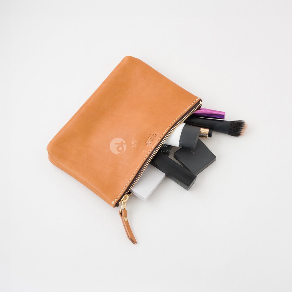 職人手作皮革長方形拉鍊收納包，淺棕色，拉鍊開口，露出部分化妝品，如唇膏、粉餅和化妝刷。