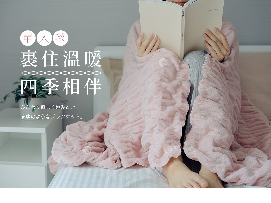 一條粉色絨毛毯，表面有立體褶皺紋理，一位女性裹著毯子，手持打開的書本，坐在床上閱讀。