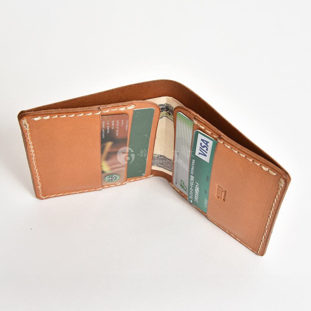 日本HERZ手工製作的棕色皮革二折式卡片夾，打開展示內部，可見卡片插槽、鈔票夾層，並插入了Visa信用卡與日圓鈔票。