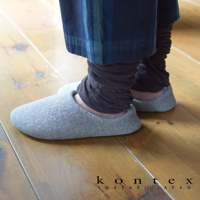 一雙灰色棉麻混紡的居家拖鞋，鞋面有細緻的織紋，搭配深棕色堆疊的襪子，展現居家舒適感。