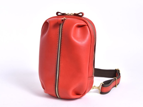 紅色皮革立體運動斜背包，配有金色拉鍊及深棕色織帶，設計簡約實用。