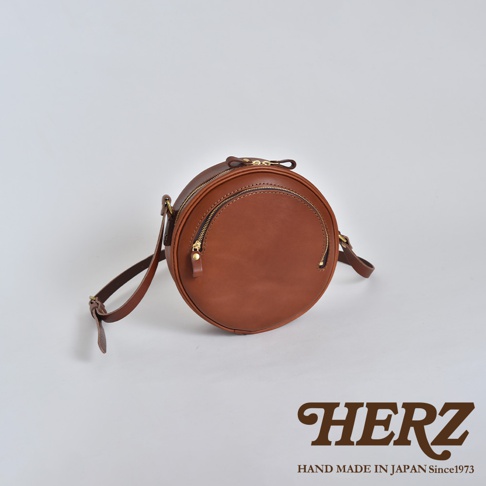 職人手作皮革小圓包，經典圓潤造型，採用棕色皮革製成，設有雙拉鍊隔層，搭配可調節式斜背帶。