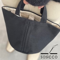 黑色三河木綿刺子織圓底水桶包，具有獨特的織紋和簡潔的提把設計，內襯為米白色。