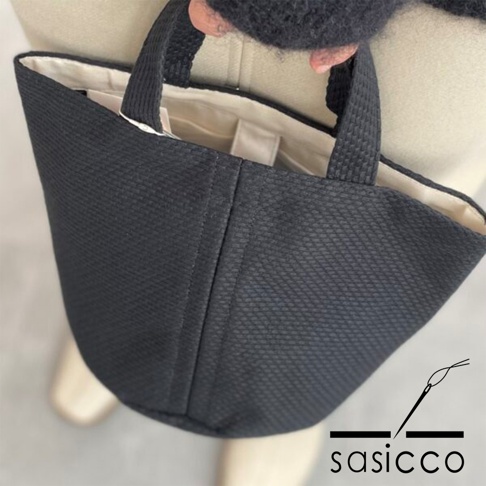 黑色三河木綿刺子織圓底水桶包，具有獨特的織紋和簡潔的提把設計，內襯為米白色。