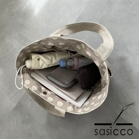 刺子織托特包，米白色帆布材質，內襯為米色圓點圖案。包內物品包含：摺疊傘、礦泉水瓶、長夾、化妝包。