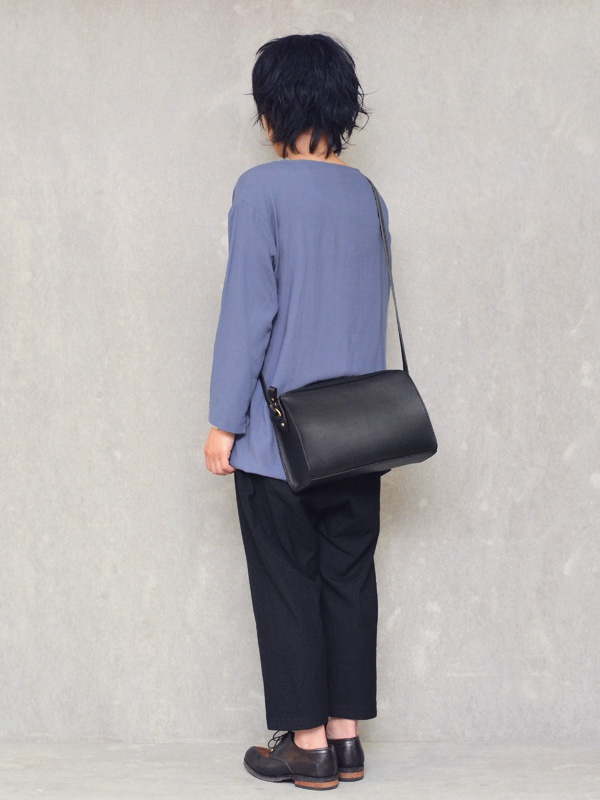 黑色皮革拉鍊單肩包，斜背於穿著藍色長袖上衣和黑色長褲的模特兒身上。