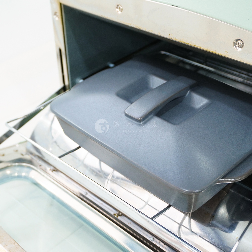 灰色陶製長方形烤盤，帶有同色系把手蓋，置於烤箱架上。