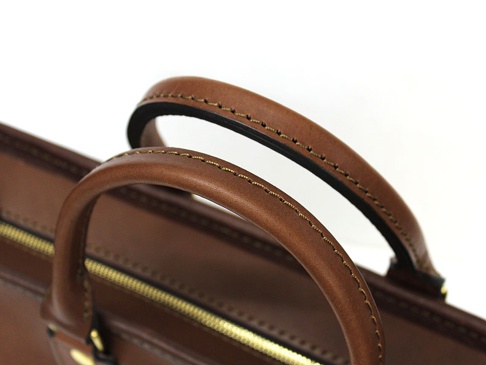 職人手作皮革兩用商務托特包 (T-7)，特寫包款的棕色皮革手把，縫線精緻，搭配金色拉鍊。