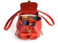 鮮紅色皮革迷你後背包，包身開口處有抽繩設計，內部裝有皮夾、零錢包與藍底白點布料。包身正面有一個翻蓋小口袋，配有束帶與金屬鎖扣。