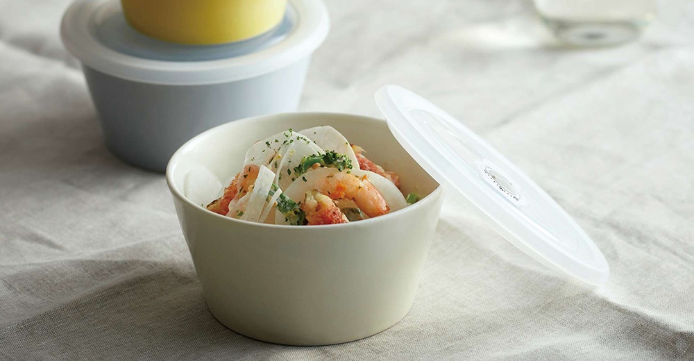 象牙色美濃燒保鮮碗，裝有鮮蝦、白蘿蔔和花椰菜沙拉，附有透明白色密封蓋，背景另有灰色和黃色保鮮碗。