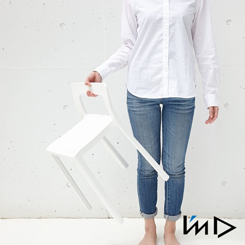 白色一體成型輕量短背椅凳，材質為塑膠，設計簡約，椅面和椅背線條流暢，椅腳呈傾斜狀，由一位身穿白色襯衫和牛仔褲的人士持握。