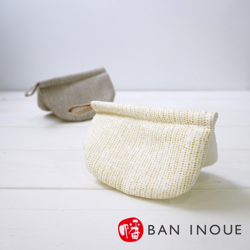 兩個 Tricot 棉麻防燙鍋套，一個為米白色織紋帶有金色線條，另一個為淺灰色織紋，皆配有皮革提環。