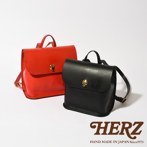 兩款職人手作皮革翻蓋迷你後背包，一款為鮮紅色，另一款為黑色，皆配有金色鎖扣及可調節肩帶，展現簡約實用的設計風格。