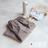 一件淺棕色棉紗混紡平口鬆緊浴裙，裙身有兩顆黑色按扣，搭配白色網狀提袋與毛巾，以及一個白色保溫瓶，整體置於六角形淺色磁磚地板上。