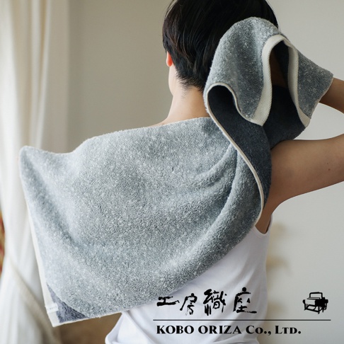 工房織座 SUFFICE 棉麻混紡雙色快乾毛巾2入組，一位女士正將灰色毛巾搭在肩上，毛巾邊緣有白色裝飾，圖片底部有工房織座 logo 和文字 KOBO ORIZA Co., LTD.