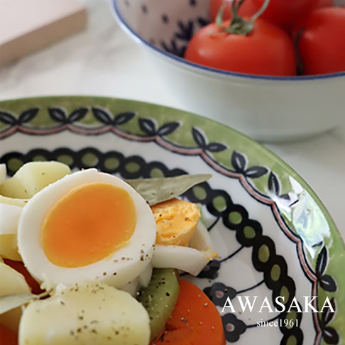 歐風淺湯盤，盤緣飾有綠色葉片和黑色圓點圖案，盤中盛有水煮蛋、馬鈴薯塊、番茄塊、紅蘿蔔片和奇異果片，撒有黑胡椒粒。