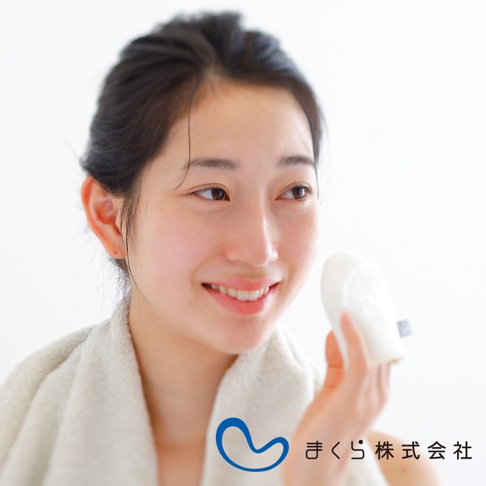 一名女子手持白色蠶絲洗臉手套，臉上掛著微笑，脖子上圍著一條白色毛巾。