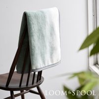 抗菌短絨舒柔雙人毯，呈現柔和的藍綠色漸層，一角為白色，邊緣有細緻的灰色滾邊，質地輕盈柔軟，披掛在木椅上。