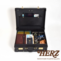 黑色皮革英倫風手提行李箱，箱內裝有平板電腦、護照、文件、錢包、摺疊傘及其他小物。箱體設有金色鎖扣及提把。