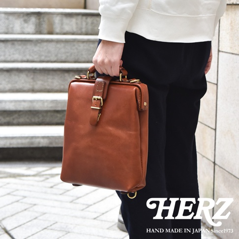 職人手作皮革迷你軟皮杜勒斯包，採用棕色鞣革皮革，設有頂部提把、可調節帶扣開合及金色五金配件。