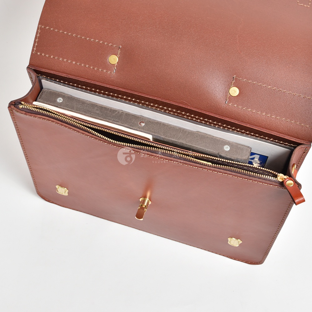 棕色皮革商務公事包，打開狀態，內部可見拉鍊隔層，裝有文件和筆記型電腦。包身有黃銅色金屬扣件和拉鍊。