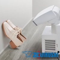 一雙米白色皮革低跟繫帶鞋，鞋頭有縫線裝飾，靠牆放置。右側為白色多功能智慧烘乾機，有可調節角度的噴嘴和側面散熱孔。