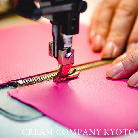 粉紅色皮革材質的手機包，正在由職人使用縫紉機縫製拉鍊，展示精細工藝。