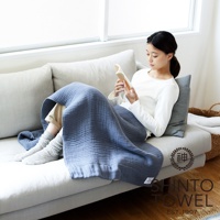 一位女性在沙發上蓋著藍色雙面紗布浴巾閱讀。