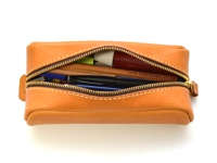 職人手作皮革圓角收納筆袋，採用淺棕色皮革製成，拉鍊部分露出多支筆、鉛筆和一支毛筆。