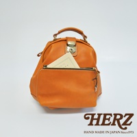 橙色皮革手提後背包，具有頂部提把、金色金屬鎖扣及拉鍊前袋，袋中插有一本淺色書籍。