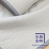 象牙白色天絲棉絎縫單人毯，表面有著流線型的壓紋圖案，邊緣為淺灰色滾邊。右下角印有藍色框線的金色日文「京都金桝」及英文「kyoto kanemasu」字樣，並標示「SINCE 1932」。